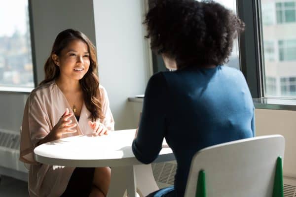 two women facing each other across the table in conversation representing the concept of holding space for each other